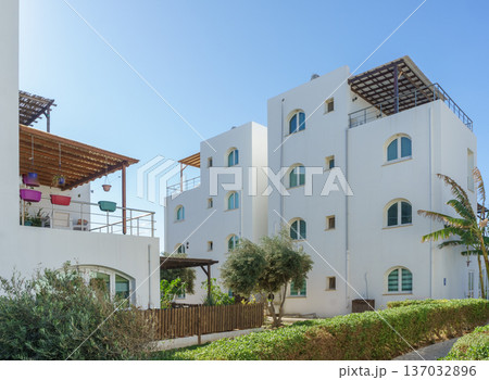 Charming white buildings nestled among greenery on a sunny day in a coastal area. Charming white buildings nestled among greenery on a sunny day in a coastal area. 137032896