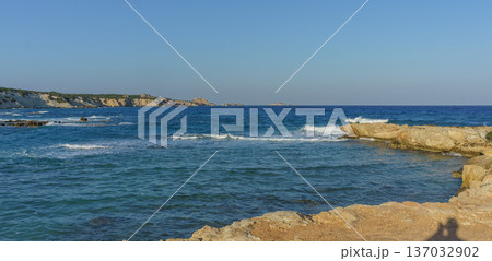 Tranquil coastal view at sunset with gentle waves lapping against rocky shores. Tranquil coastal view at sunset with gentle waves lapping against rocky shores. 137032902