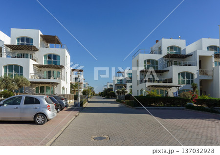 Modern coastal residences line the tranquil street on sunny day near the shore. 137032928