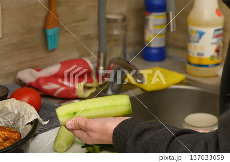 Close-Up of Hands Peeling Cucumber on Wooden Cutting Board Close-Up of Hands Peeling Cucumber on Wooden Cutting Board 137033059