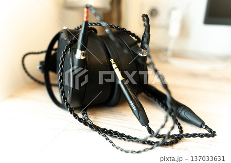 Black monitor headphones on a table with audiophile wires, representing high-quality music listening. Professional audio equipment for studio monitoring, critical listening, and immersive sound Black monitor headphones on a table with audiophile wires, representing high-quality music listening. Professional audio equipment for studio monitoring, critical listening, and immersive sound 137033631