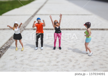 Miniature dancers raise arms energetically on outdoor concrete surface Miniature dancers raise arms energetically on outdoor concrete surface 137034091