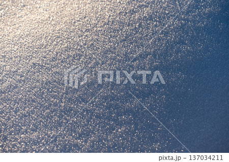 Texture of snow in warm sunlight, creating a beautiful frozen nature background. The soft winter light highlights the delicate crystalline structure and pristine white surface. 137034211