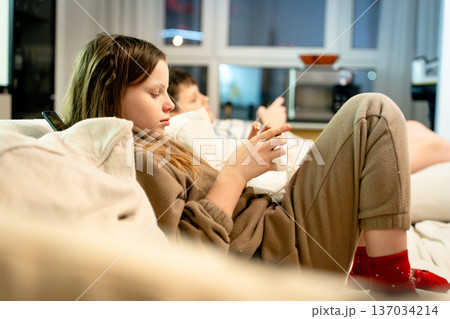 Two children, a boy and a girl, siblings on a sofa at home, deeply focused on a smartphone playing games. Concept of phone addiction, digital dependency, and modern childhood. Two children, a boy and a girl, siblings on a sofa at home, deeply focused on a smartphone playing games. Concept of phone addiction, digital dependency, and modern childhood. 137034214