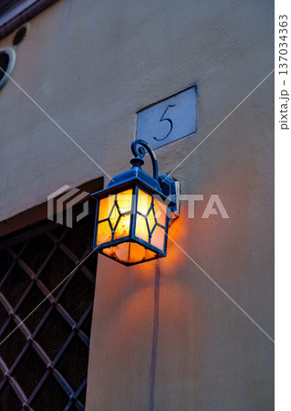 Lamp shines on wall near house number five in evening light Lamp shines on wall near house number five in evening light 137034363