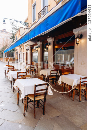 Outdoor cafe seating with tables and chairs on a quiet street in the daytime 137034431