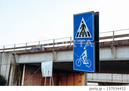 Traffic signs show pedestrian and bicycle paths near a highway overpass in the city 137034432