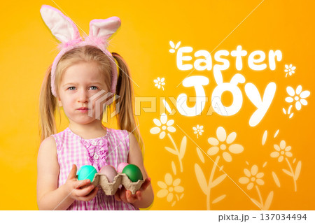 Child holds Easter eggs with bunny ears and yellow background showing joyful message about Easter 137034494