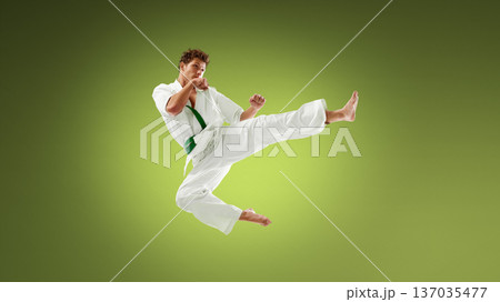 Young karate athlete delivering powerful side kick in mid air wearing white gi and green belt. Young karate athlete delivering powerful side kick in mid air wearing white gi and green belt. 137035477