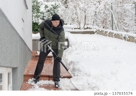 55 year old man in winter clothes removes snow with shovel on house steps after snowfall 55 year old man in winter clothes removes snow with shovel on house steps after snowfall 137035574