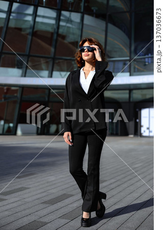 Confident Businesswoman Adjusting Sunglasses While Walking In City 137036673