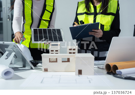 Two colleagues discussing data working and tablet, laptop with on Construction Site project, green energy and solar panel concept. Two colleagues discussing data working and tablet, laptop with on Construction Site project, green energy and solar panel concept. 137036724