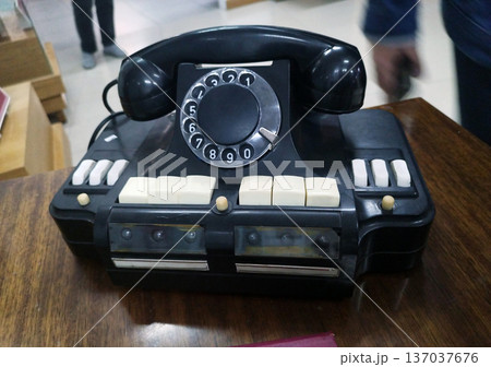 Vintage black rotary dial telephone with white keys, resting on a dark wooden table. Slightly blurred, in the background. Vintage black rotary dial telephone with white keys, resting on a dark wooden table. Slightly blurred, in the background. 137037676