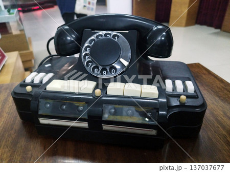 Vintage black rotary telephone with white keys sits on a dark wooden table. The image is slightly blurred in the background Vintage black rotary telephone with white keys sits on a dark wooden table. The image is slightly blurred in the background 137037677