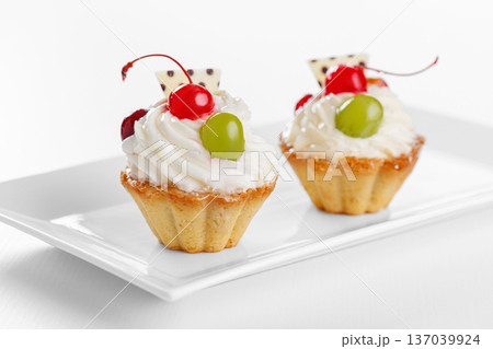 Beautiful cream cakes with cherries and grapes on a plate on a white background 137039924