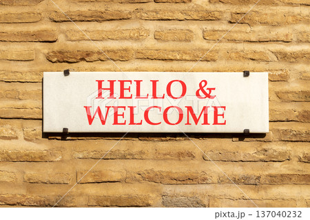 Hello and welcome symbol. Concept words Hello and welcome on beautiful big white sign plate. Beautiful old brown brick wall background. Business hello and welcome concept. Copy space. Hello and welcome symbol. Concept words Hello and welcome on beautiful big white sign plate. Beautiful old brown brick wall background. Business hello and welcome concept. Copy space. 137040232