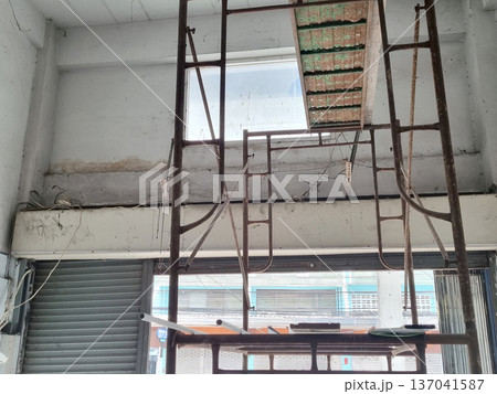 Metal scaffolding inside a building under renovation. Industrial construction site with concrete walls, exposed wiring, and rolling metal shutter door. Interior building maintenance and repair. 137041587