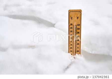 Wooden thermometer measuring freezing temperature in snow 137042361