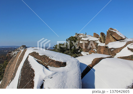 Snow covered rock formations under clear blue sky. Winter landscape of natural rock park for travel and nature exploration. Krasnoyarsk Stolby park Snow covered rock formations under clear blue sky. Winter landscape of natural rock park for travel and nature exploration. Krasnoyarsk Stolby park 137042605