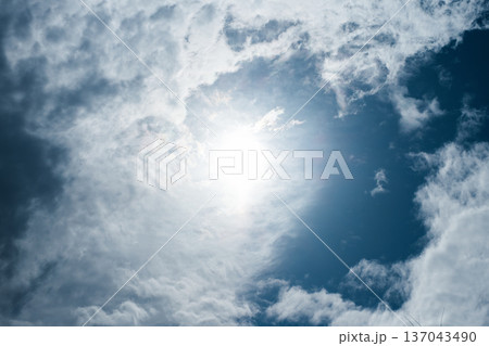 青空の中央に輝く太陽と流れる白い雲 137043490