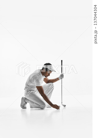 Golfer kneeling and placing ball on tee on white background. 137044304