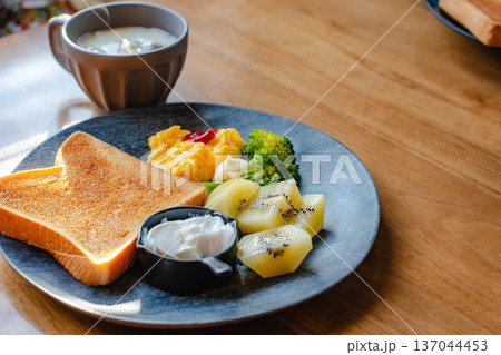 木のテーブルに並ぶトーストとスクランブルエッグとキウイの朝食ワンプレートとスープ 137044453