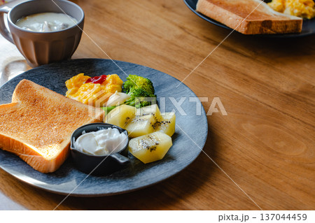 木のテーブルに並ぶ朝食プレート トーストと卵料理とフルーツとスープ 137044459