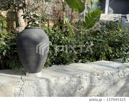 Earthenware pot on stone wall surrounded by lush greenery in outdoor garden setting 137045325