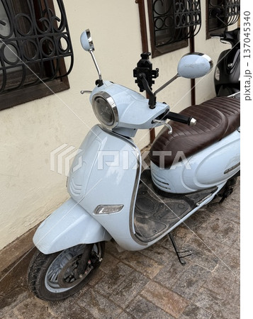 Light blue scooter parked on urban street next to building wall, ideal for transportation themes Light blue scooter parked on urban street next to building wall, ideal for transportation themes 137045340