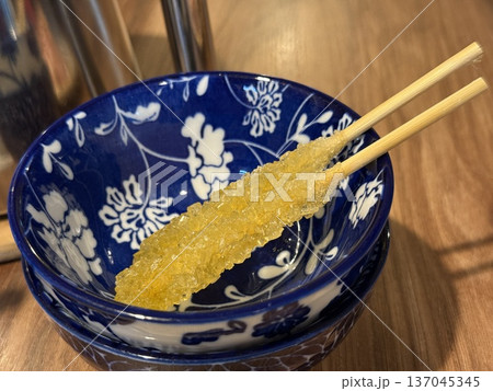 Rock candy in ornate blue bowl on wooden table setting, emphasizing artisanal sweet treat 137045345