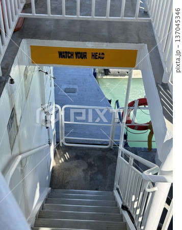 Staircase on ship deck with watch your head sign and safety equipment in bright sunlight Staircase on ship deck with watch your head sign and safety equipment in bright sunlight 137045346