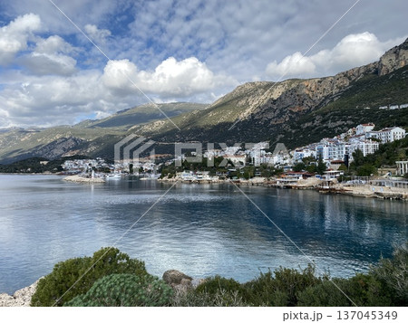 Coastal town with mountainous backdrop under cloudy sky, perfect for travel background or adventure Coastal town with mountainous backdrop under cloudy sky, perfect for travel background or adventure 137045349