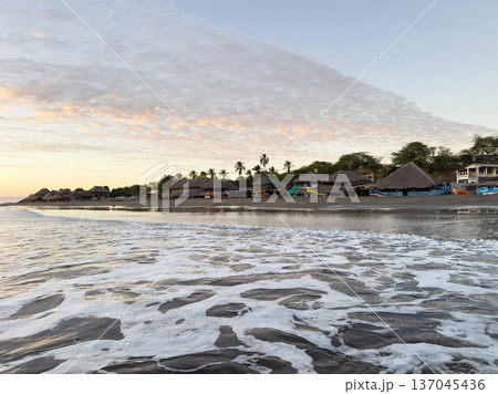 Sunset at the beach with huts and fishing boats in the distance 137045436