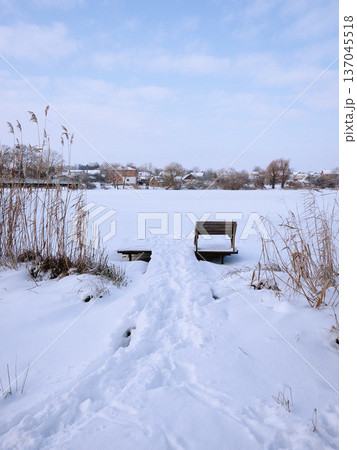 A path leading to a single bench in front of a lake in winter A path leading to a single bench in front of a lake in winter 137045518