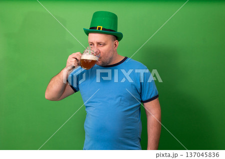 Man drinking beer while wearing green leprechaun hat. St. Patricks Day festive toast. Irish holiday celebration and pub tradition photography Man drinking beer while wearing green leprechaun hat. St. Patricks Day festive toast. Irish holiday celebration and pub tradition photography 137045836