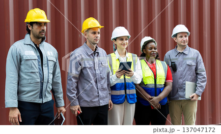 Diverse construction team wearing safety helmets and reflective vests standing in front of shipping container, industrial workers teamwork concept, engineering inspection and site management Diverse construction team wearing safety helmets and reflective vests standing in front of shipping container, industrial workers teamwork concept, engineering inspection and site management 137047172