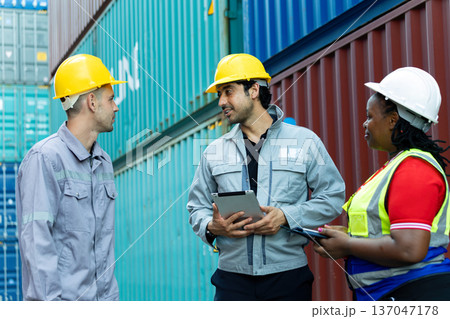 Construction engineers wearing safety helmets discussing project plan with tablet at shipping container yard, industrial teamwork, logistics coordination and site management concept 137047178