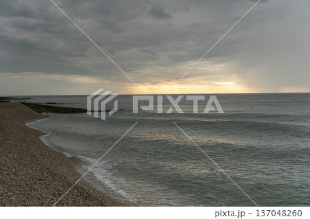 Pebble beach, Black Sea coastline under dramatic cloudy sky with soft light near horizon, wide coastal perspective, muted gray blue tones. Image supports tourism, wellness communication 137048260