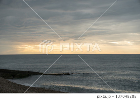 Pebble beach, Black Sea coastline under dramatic cloudy sky with soft light near horizon, wide coastal perspective, muted gray blue tones. Image supports tourism, wellness communication 137048288