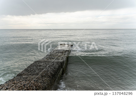 Concrete pier extending into calm sea, overcast sky, muted blue and gray tones creating minimalist coastal composition. Tourism marketing, sustainability concepts, travel branding 137048296