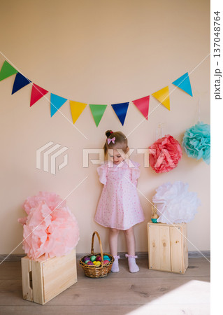 Cute little girl wearing pink dress holding basket with painted Easter eggs 137048764