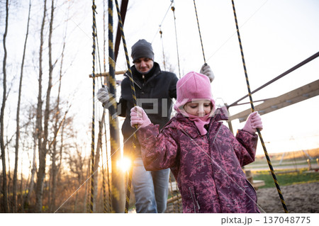 Father and daughter play on swings at sunset in a park during winter 137048775