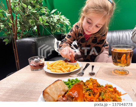 Child enjoys fries with ketchup at a diner while food is served on the table 137048778