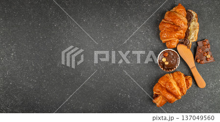 Chocolate croissants with hazelnut spread and knife on dark stone background 137049560