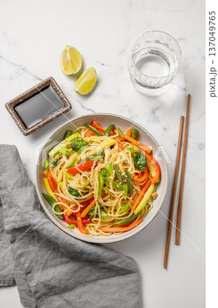 Stir fry wok noodles with vegetables in a plate on a light marble background with chopsticks Stir fry wok noodles with vegetables in a plate on a light marble background with chopsticks 137049765