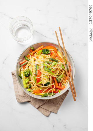 Vegetarian wok noodles with vegetables in a plate on a light marble background with chopsticks Vegetarian wok noodles with vegetables in a plate on a light marble background with chopsticks 137049766