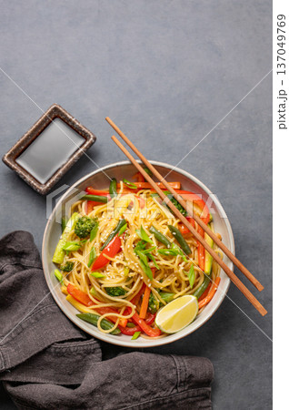 Stir fry wok noodles with vegetables in a plate on a dark background with chopsticks Stir fry wok noodles with vegetables in a plate on a dark background with chopsticks 137049769