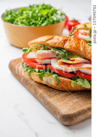 Two croissant sandwiches with ham, mozzarella cheese and arugula on a wooden board Two croissant sandwiches with ham, mozzarella cheese and arugula on a wooden board 137049782