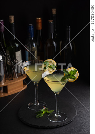 Elegant cocktail two glasses of limoncello spritz, garnished with fresh lemon slices and mint sprigs against a refined bar background with cocktail tools 137050480