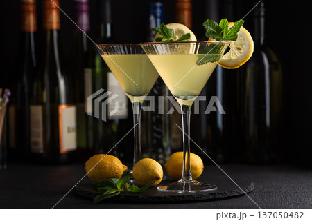 Elegant cocktail two glasses of limoncello spritz, garnished with fresh lemon slices and mint sprigs against a refined bar background with cocktail tools Elegant cocktail two glasses of limoncello spritz, garnished with fresh lemon slices and mint sprigs against a refined bar background with cocktail tools 137050482